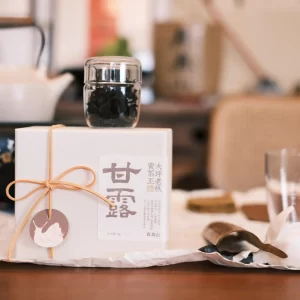 This Ganlu Phoenix Dancong Oolong from Guangdong comes in beautifully designed packaging that highlights key details, including its raw leaf origin from Daping Village tea estate in Fenghuang Town. The single-brew dry tea leaves are displayed in a clear glass jar, allowing tea enthusiasts to appreciate the shape and quality of the leaves before brewing.